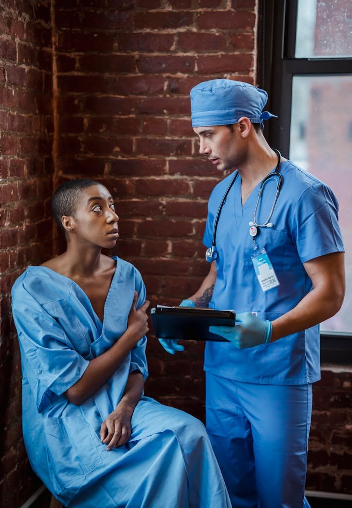 Calm doctor in blue uniform standing and talking diagnosis to African American woman patient in hallway of clinic in daytime