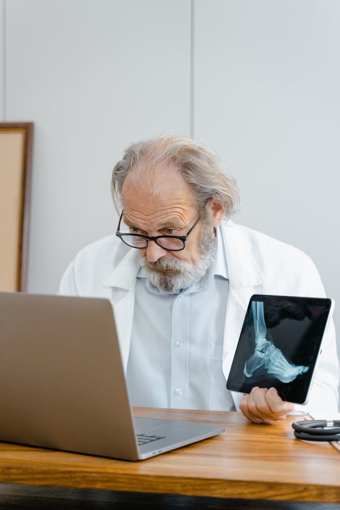 services-04 Senior doctor analyzing a foot X-ray while working on a laptop in a medical office.